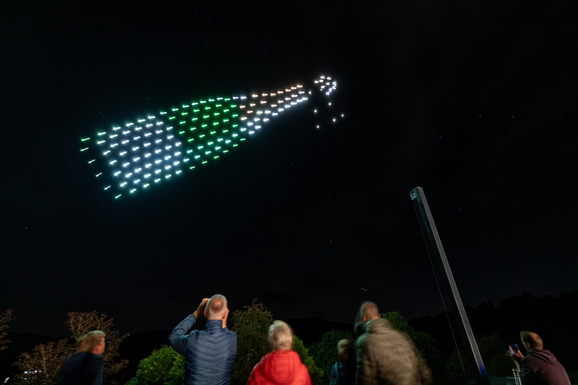 A champagne bottle in green and white drones, spraying, over the crowd